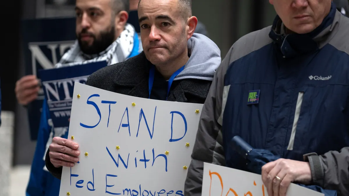 Individuals hold up signs, including one that says "stand with fed employees."