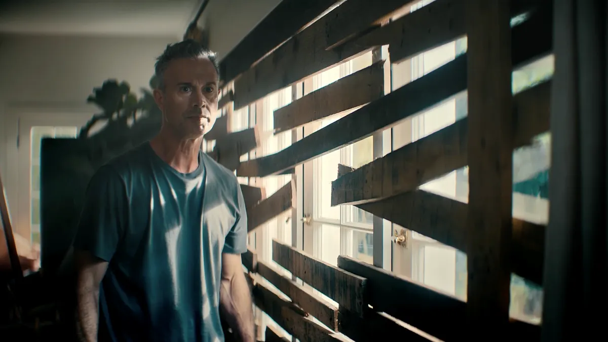 Actor Freddie Prinze Jr, wearing a dark gray shirt,, boards a window shut with wooden planks in a video for DoorDash.