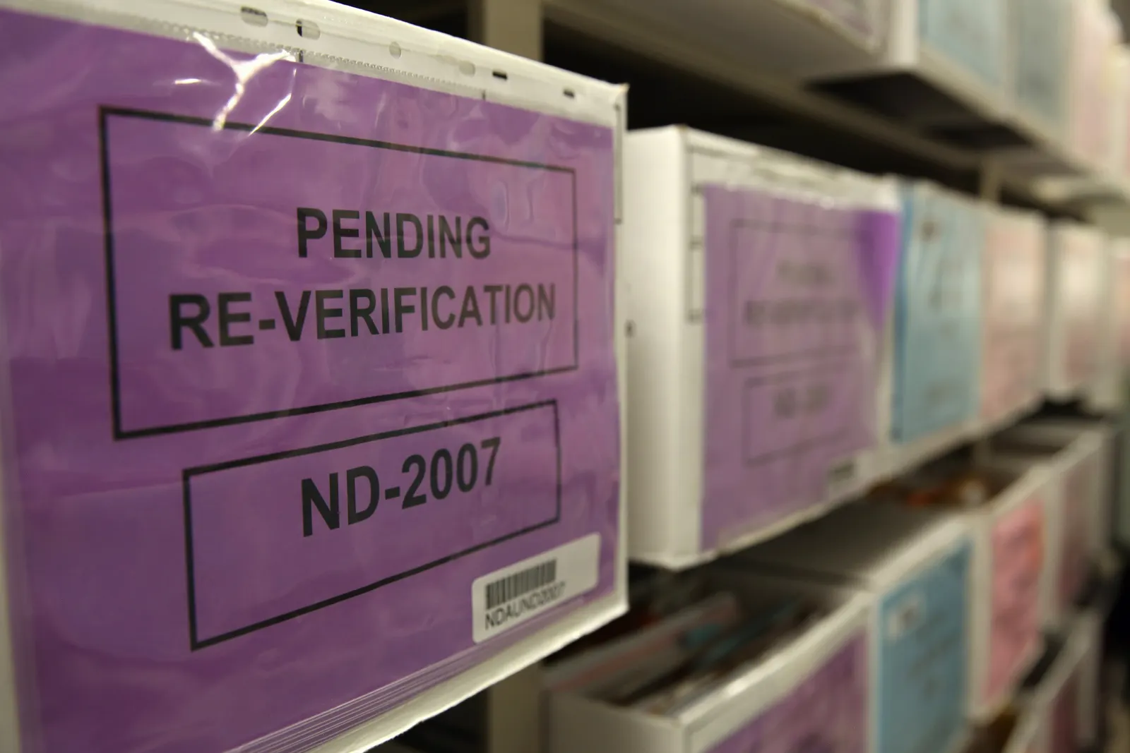 Rows of boxes sit on a shelf. The closest one bears a sign that reads "pending re-verification."
