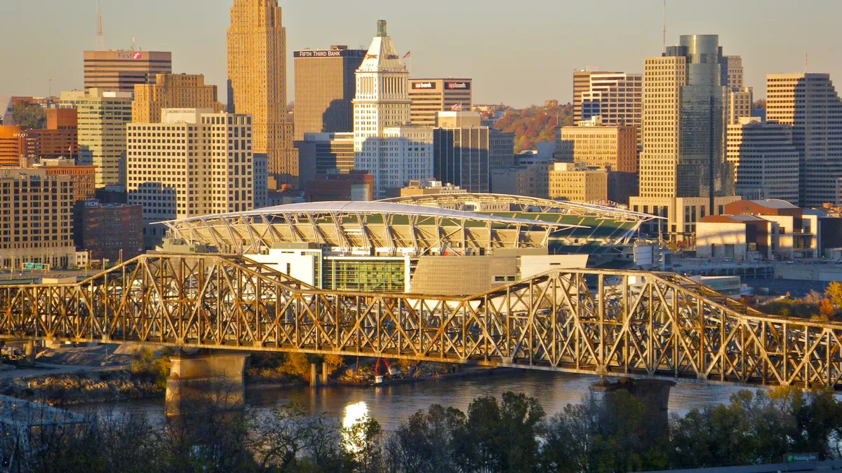 A double humped bridge bathed in yellow light spans a river, with a cityscape in the background.