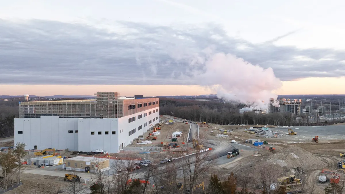 Steam rising from a power plant with construction equipment in the foreground.