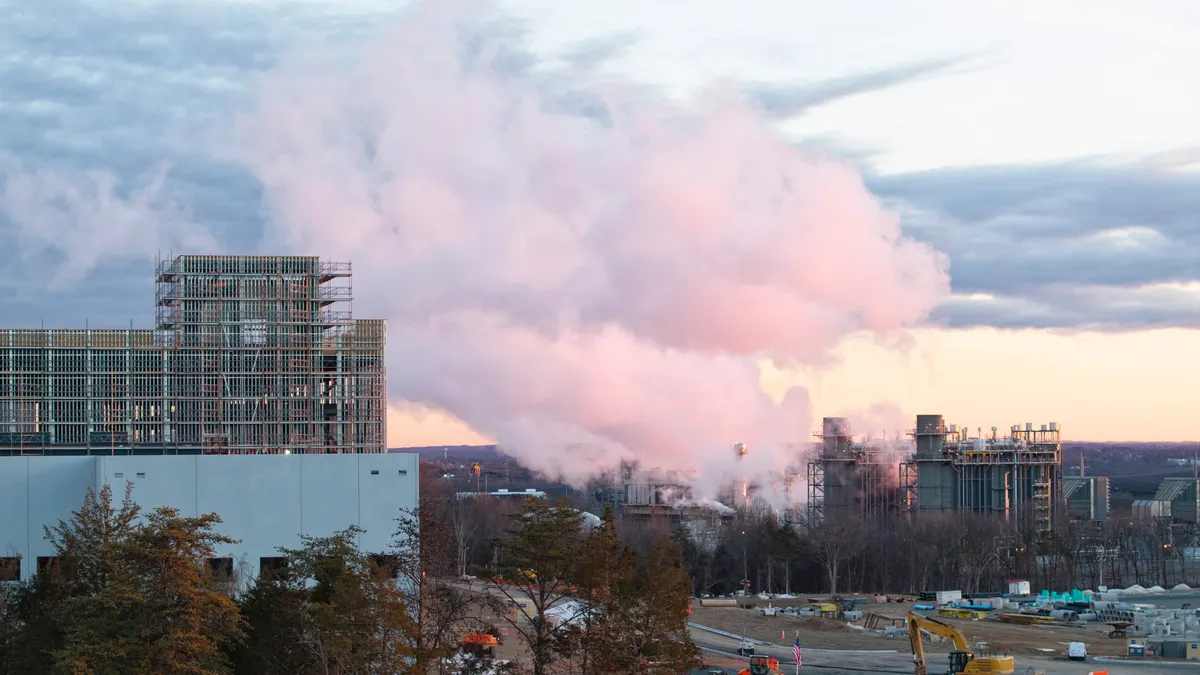 Steam rises from a power plant with construction equipment in the foreground.