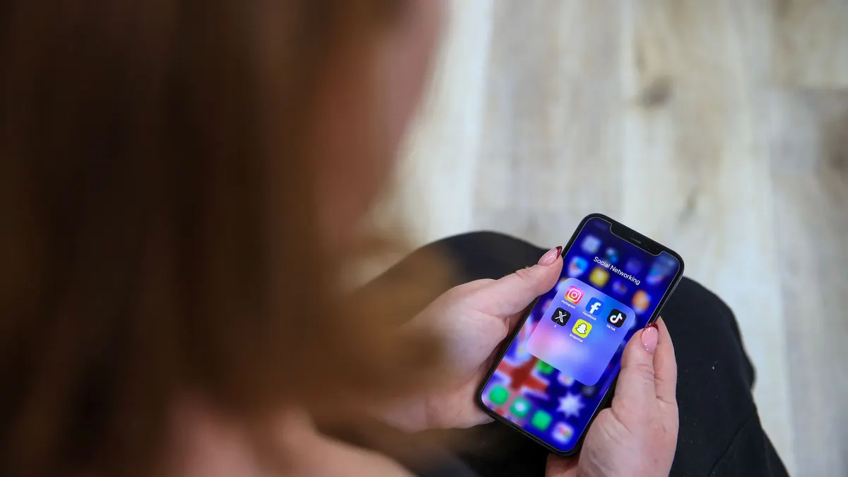 A woman holds a phone displaying social media apps.