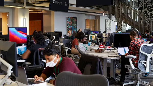 People wearing masks and sitting at their desks in front of their Apple computers.