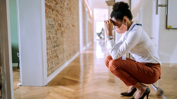 A masked Black person squats in distress in their workplace hallway