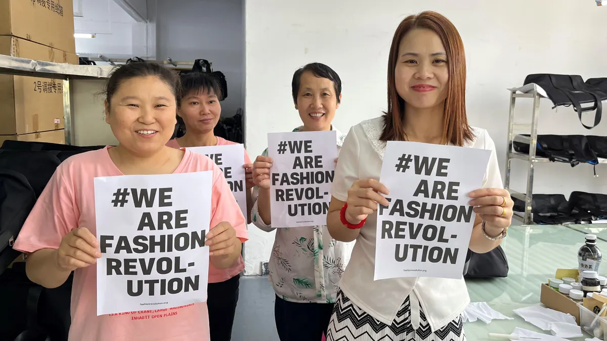 Four people stand next to each other holding signs that read #We Are Fashion Revolution