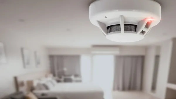 A carbon monoxide detector hangs above a hotel bed.