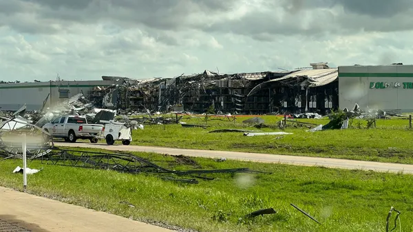 The ruins of a destroyed Dollar Tree warehouse sits on a grass lawn.
