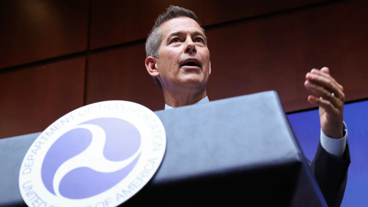 Transportation Secretary Sean Duffy, in a blue suit and tie, gestures from a podium.