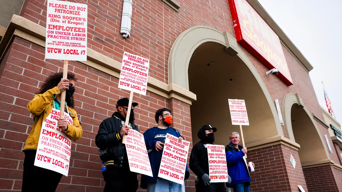 People holding white signs with red letters outside a red brick building