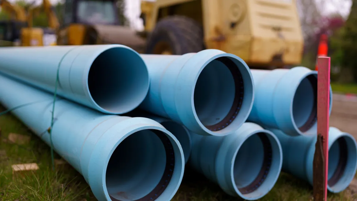 Blue pipes are stacked in front of a yellow bulldozer.